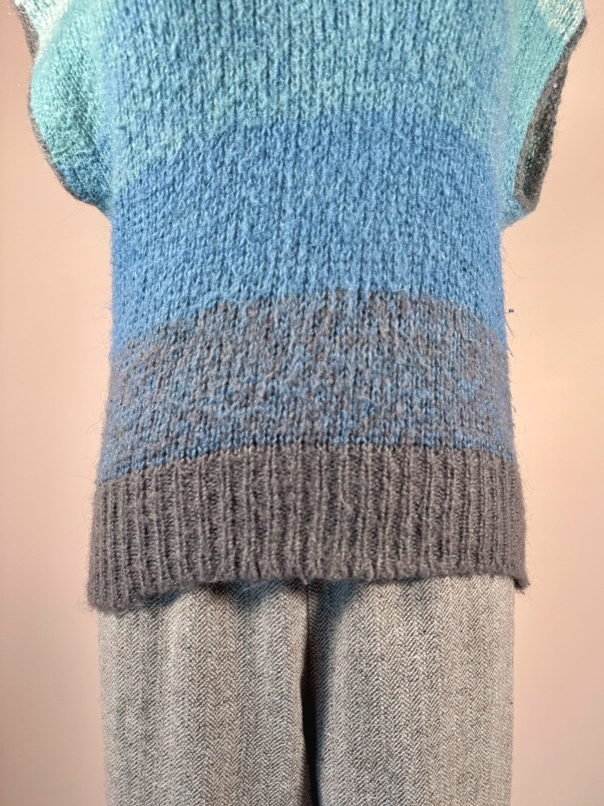 A women's blue mohair sweater vest featuring a gradient design, paired with light gray patterned pants, reflecting a 1970s style.