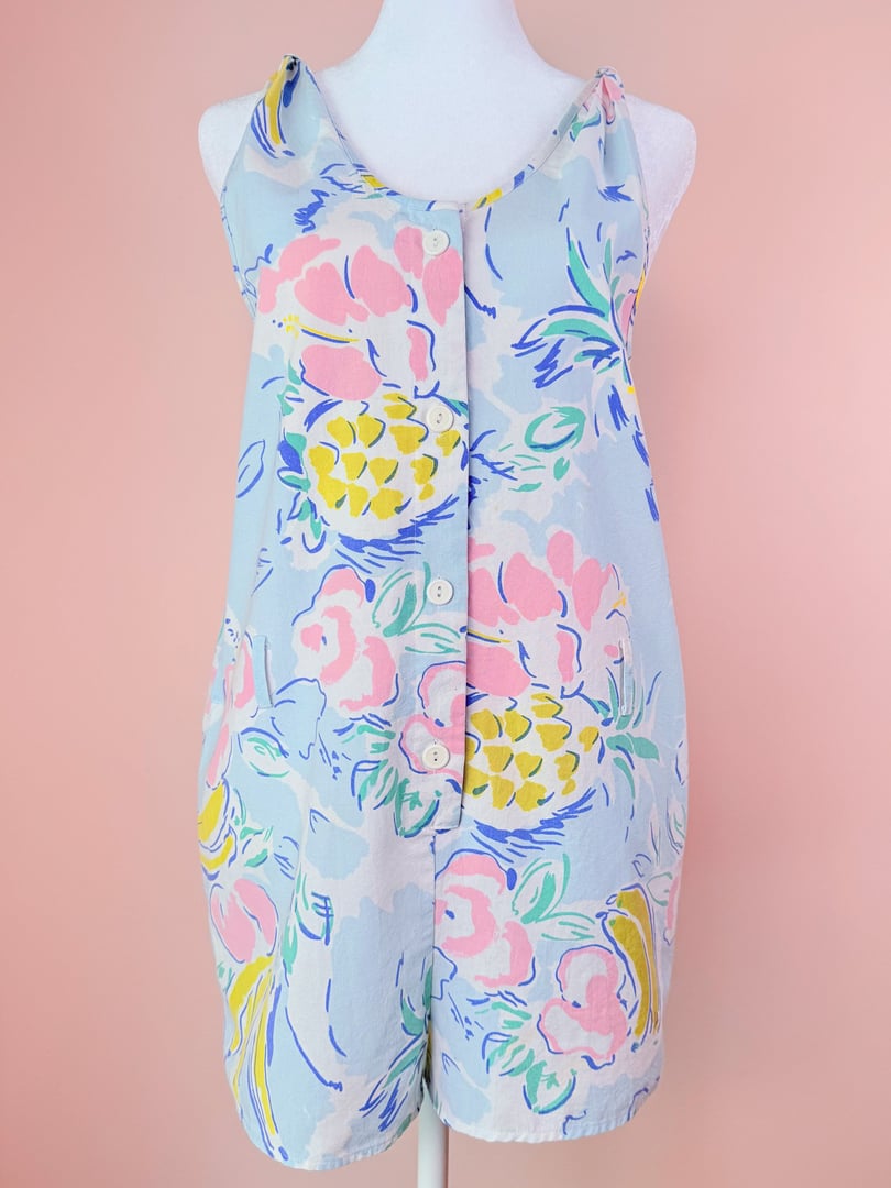 Blue 1980s women's romper featuring a colorful pineapple and floral print with button details and pockets.