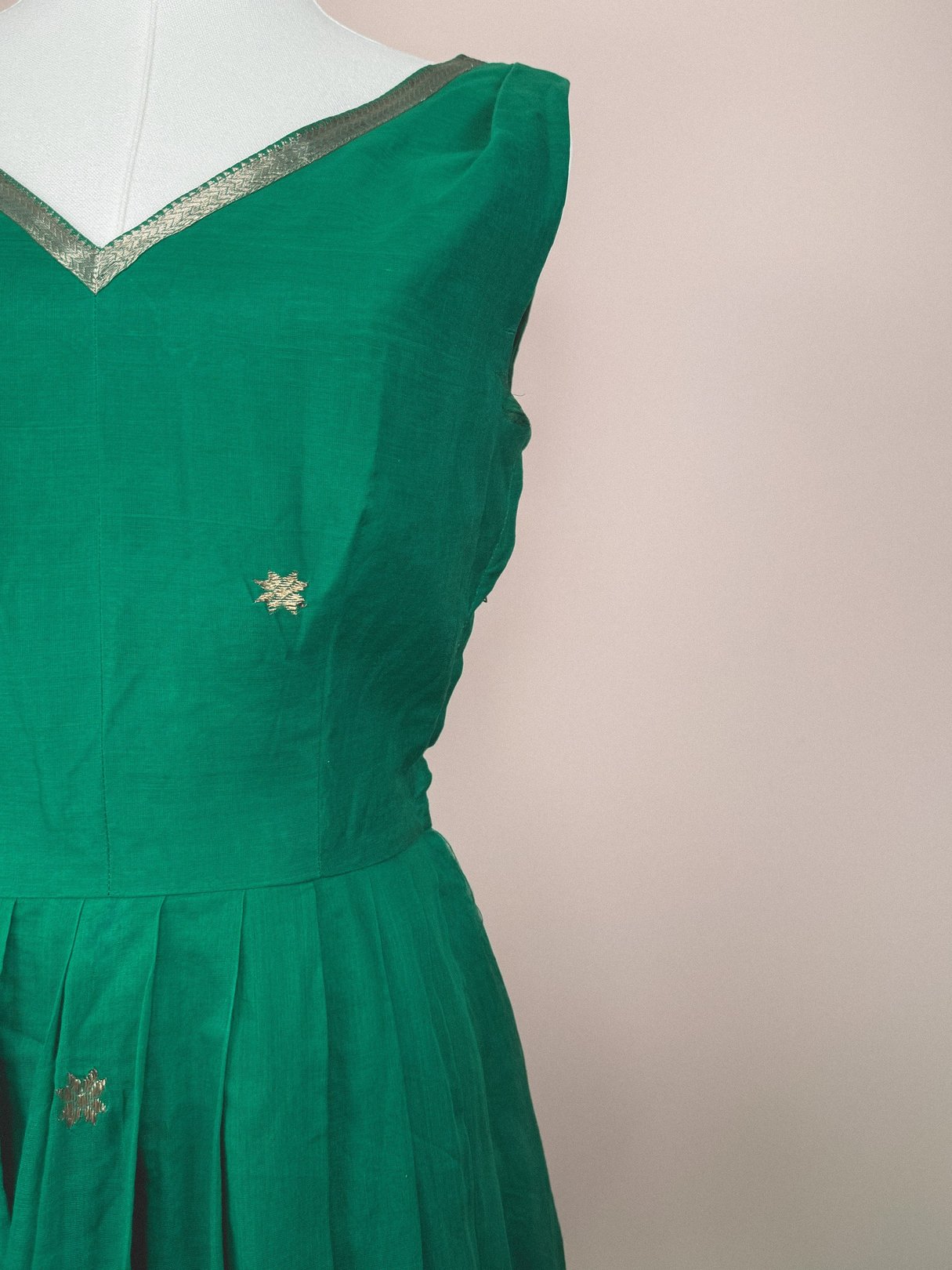 Green 1950s-style dress with a V-neckline and gold embellishments.