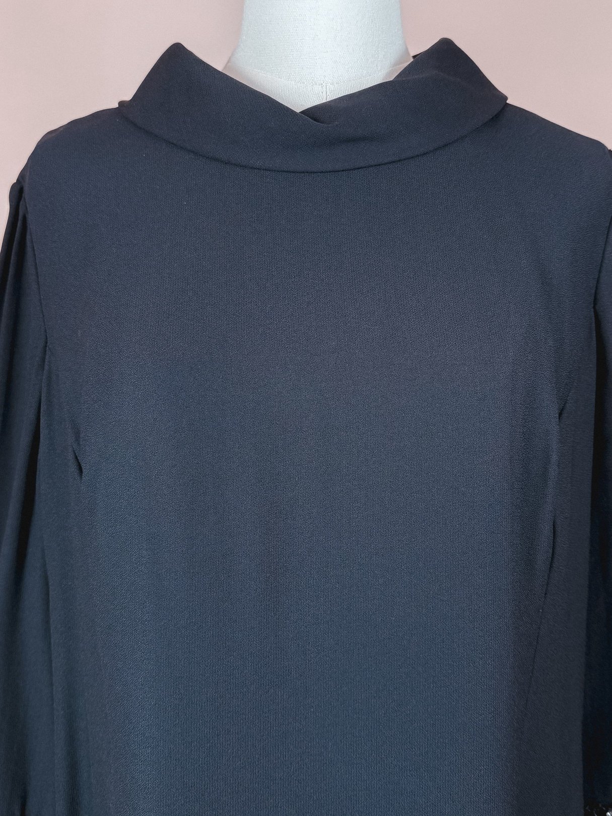 A black 1960s women's dress featuring a folded collar and long sleeves.