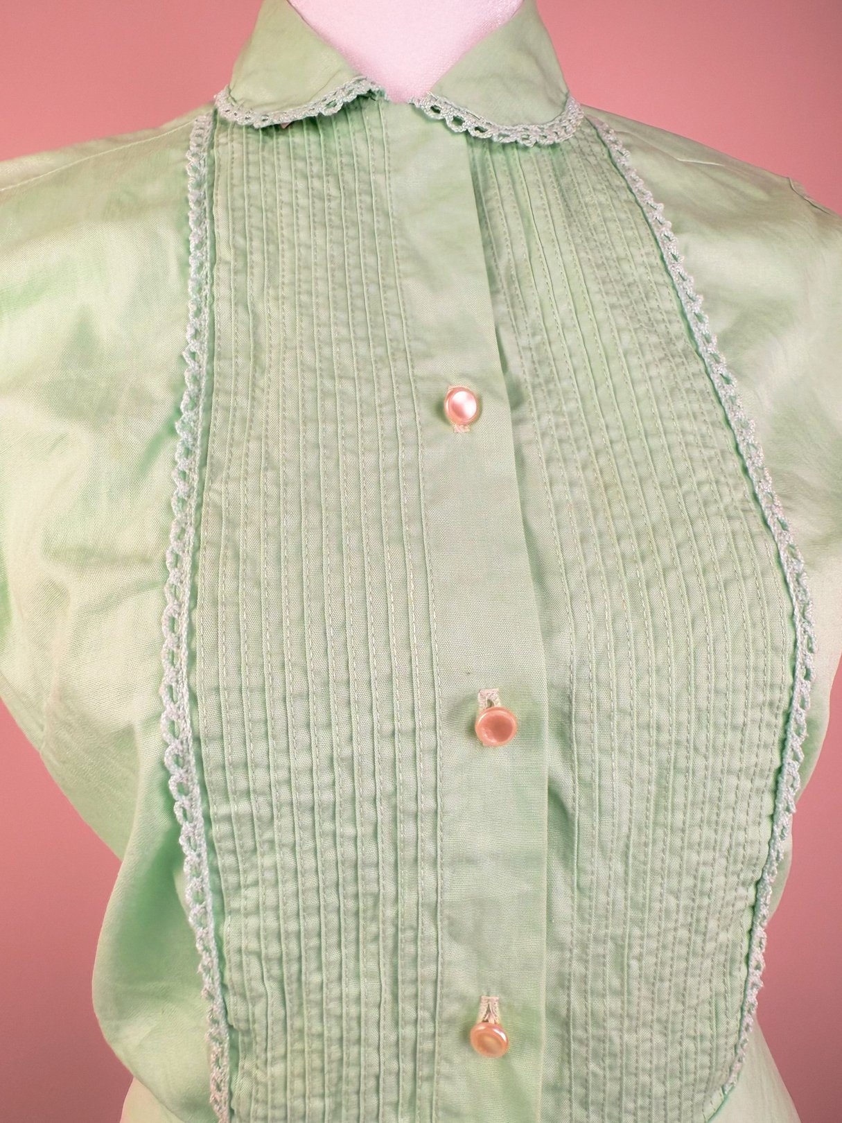 1950s mint green blouse with a pleated front and decorative buttons, designed for women.