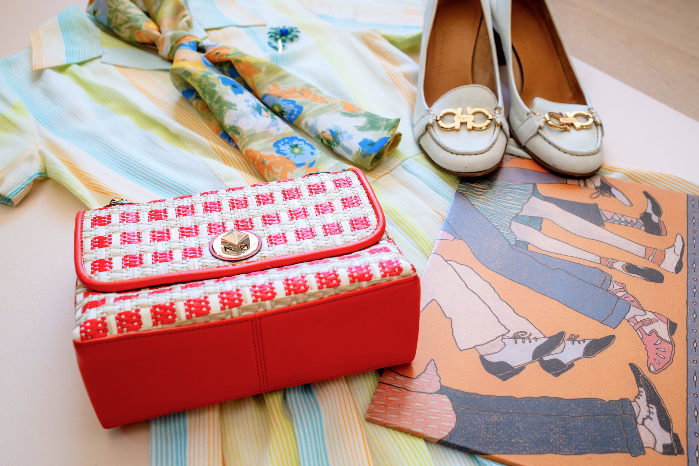 Inspired by Summer, Styled by Music gallery image: A striped short-sleeve shirt, a patterned scarf, blue and brown heeled shoes, a red and white handbag, and an illustrated fashion print are styled together in a laid-out arrangemen