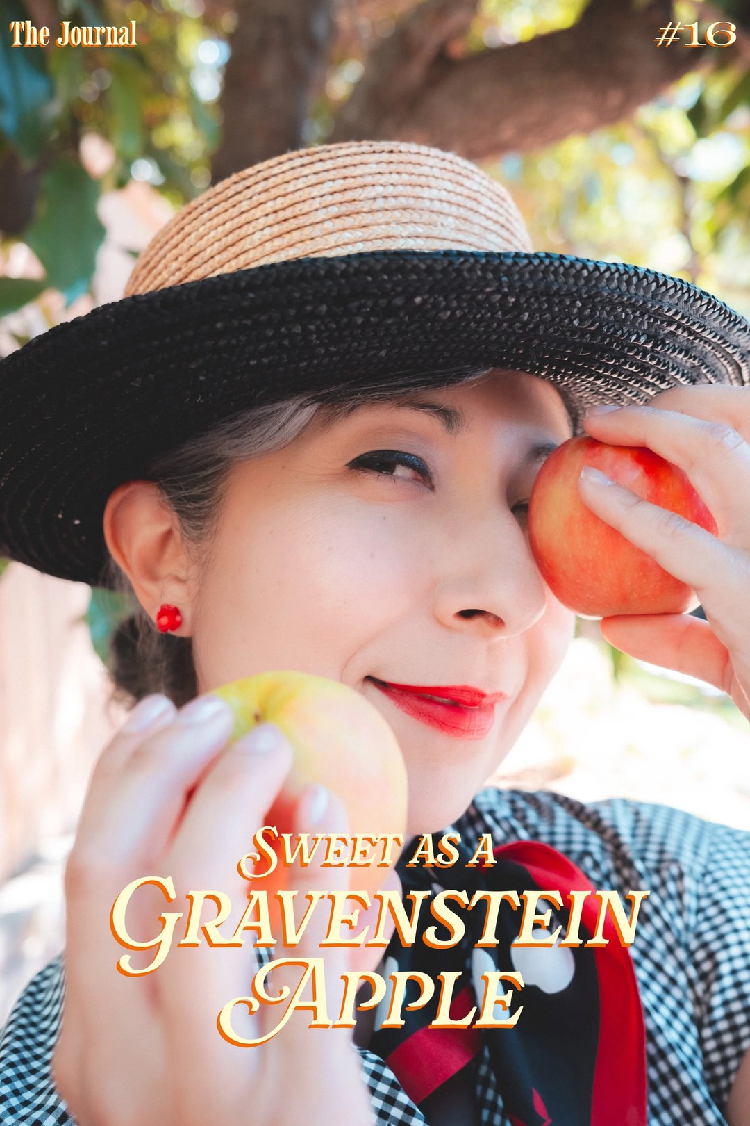 A woman holding two apples while smiling, wearing a wide-brimmed straw hat and red earrings.