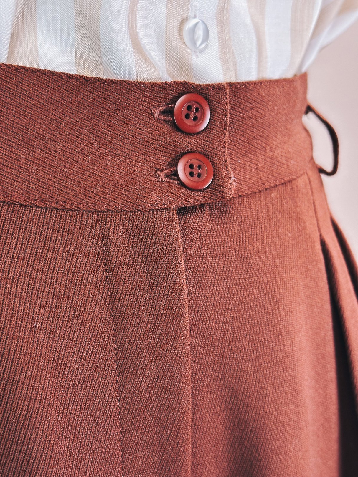 Chestnut-colored women’s pants from the 1990s featuring a high waist and two red buttons at the front.