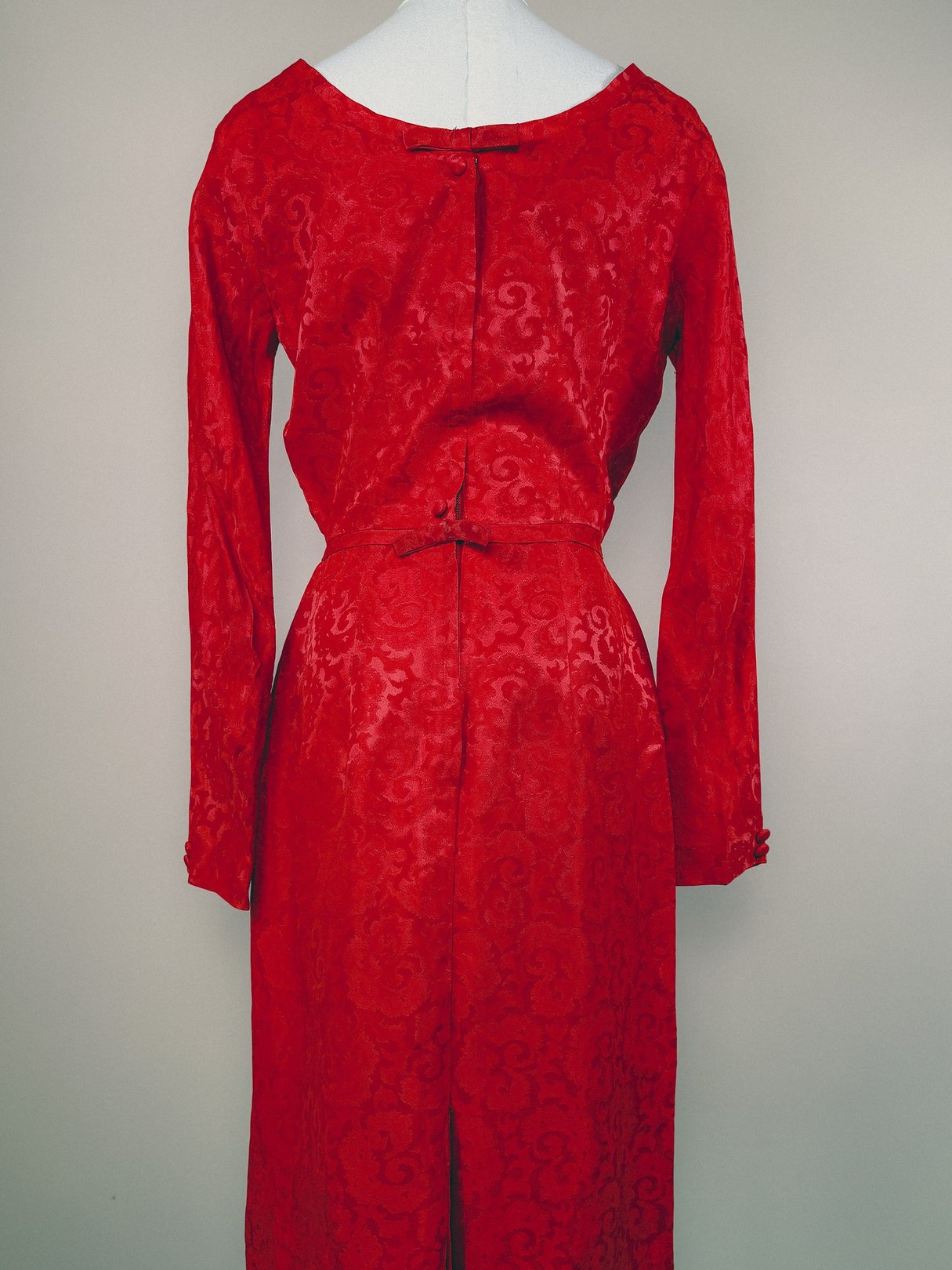 Red 1950s women's dress featuring damask fabric, long sleeves, and a fitted waist with a decorative tie closure.