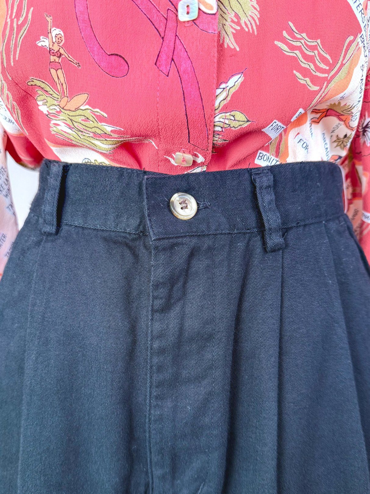 High-waisted black shorts with a front button closure and pleats, styled for women in a 1980s fashion context.