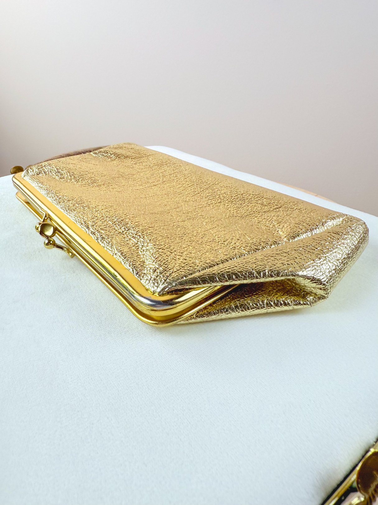 A 1950s women's gold clutch bag with a textured surface and a clasp closure.