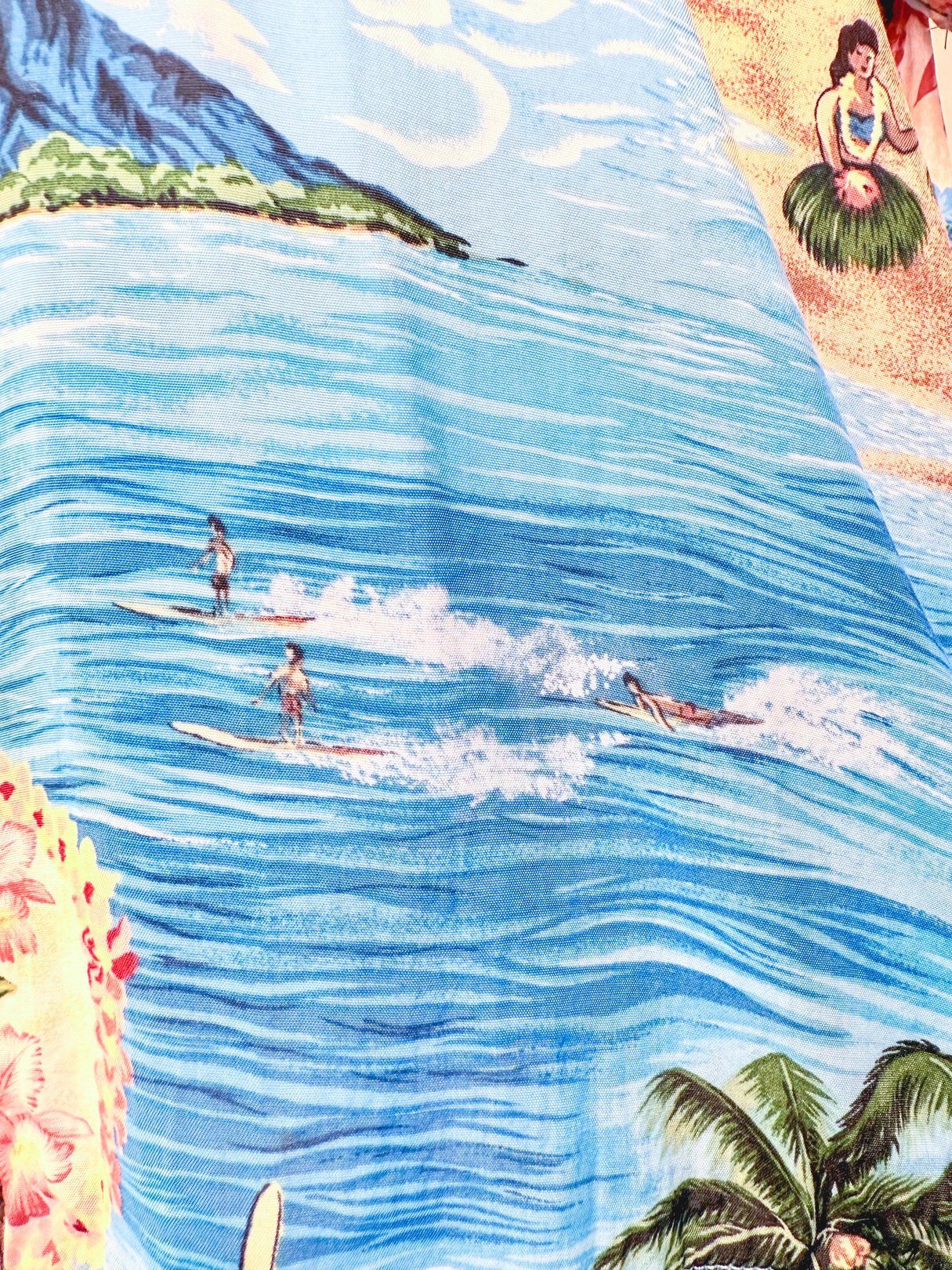 Blue 1960s Aloha Darling Top featuring a tropical beach scene with surfers and floral motifs.