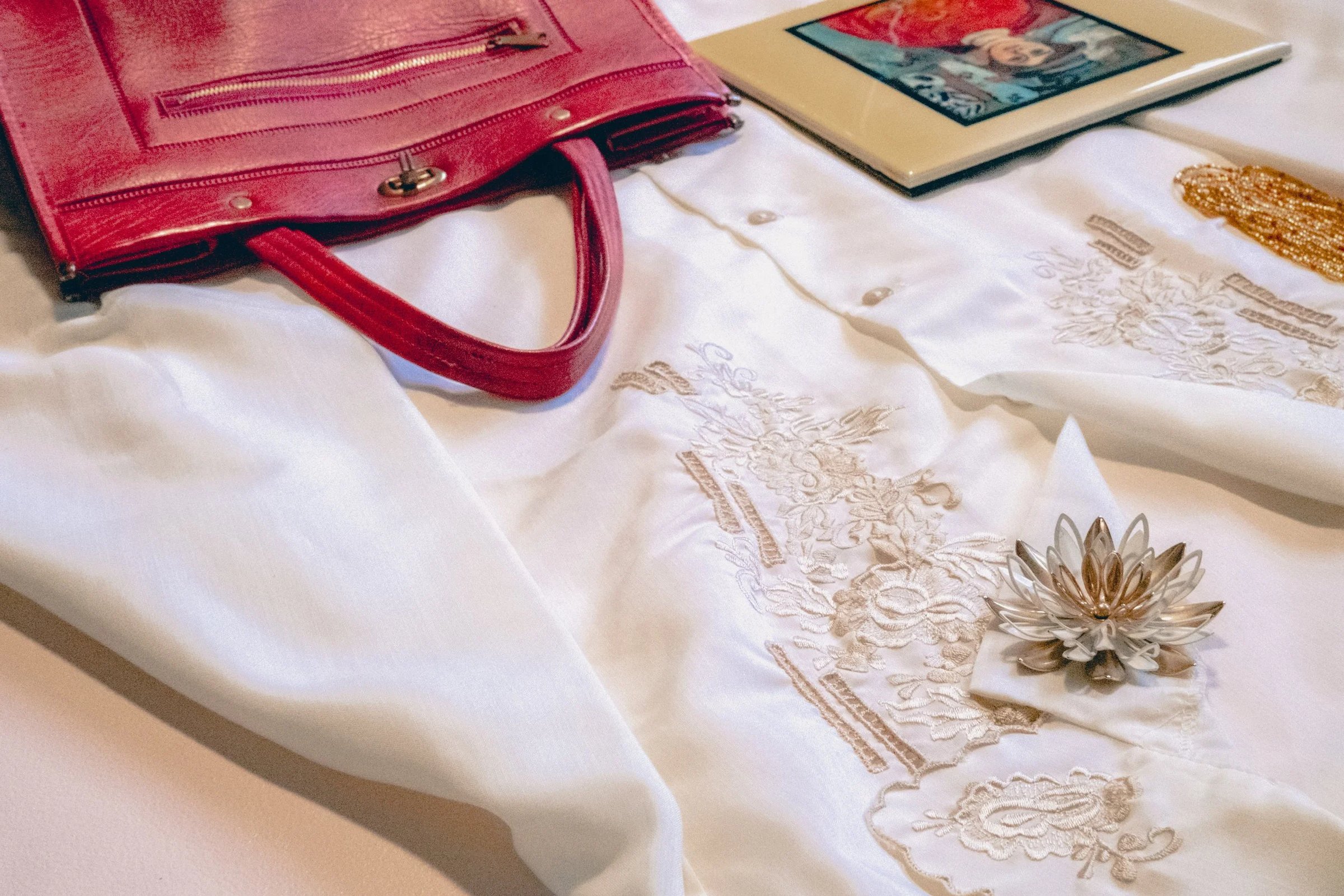 A white embroidered blouse paired with a pink handbag and a small framed artwork.