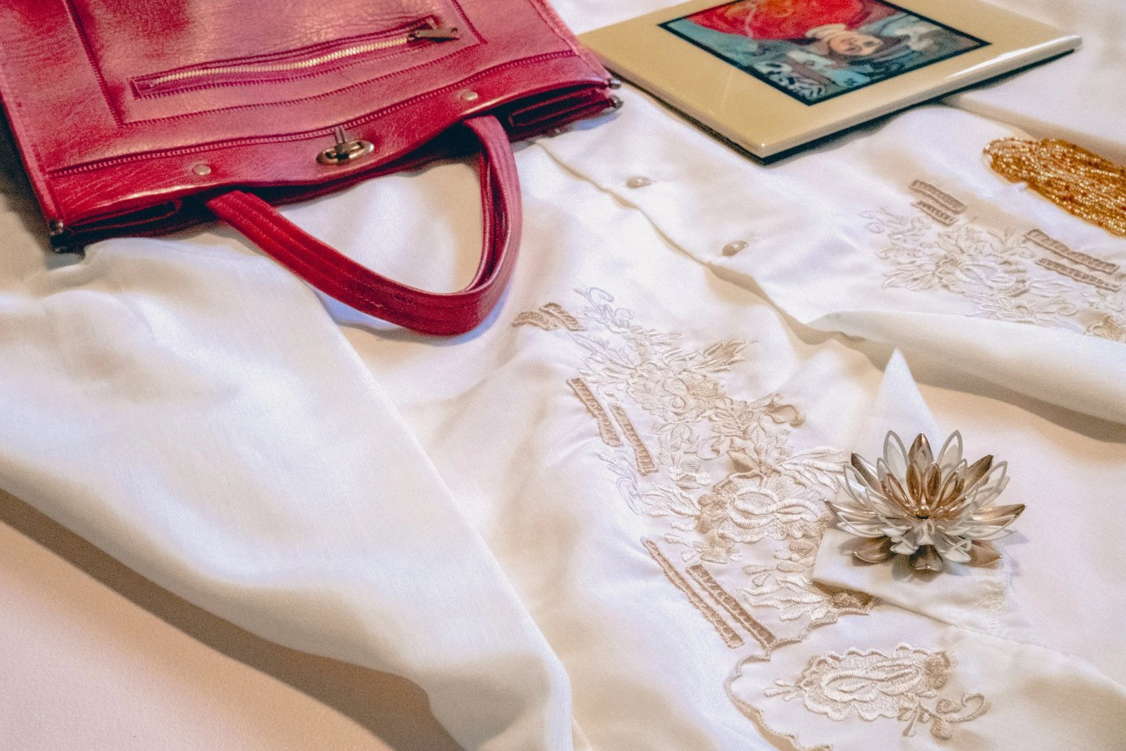 A white embroidered blouse paired with a pink handbag and a small framed artwork.