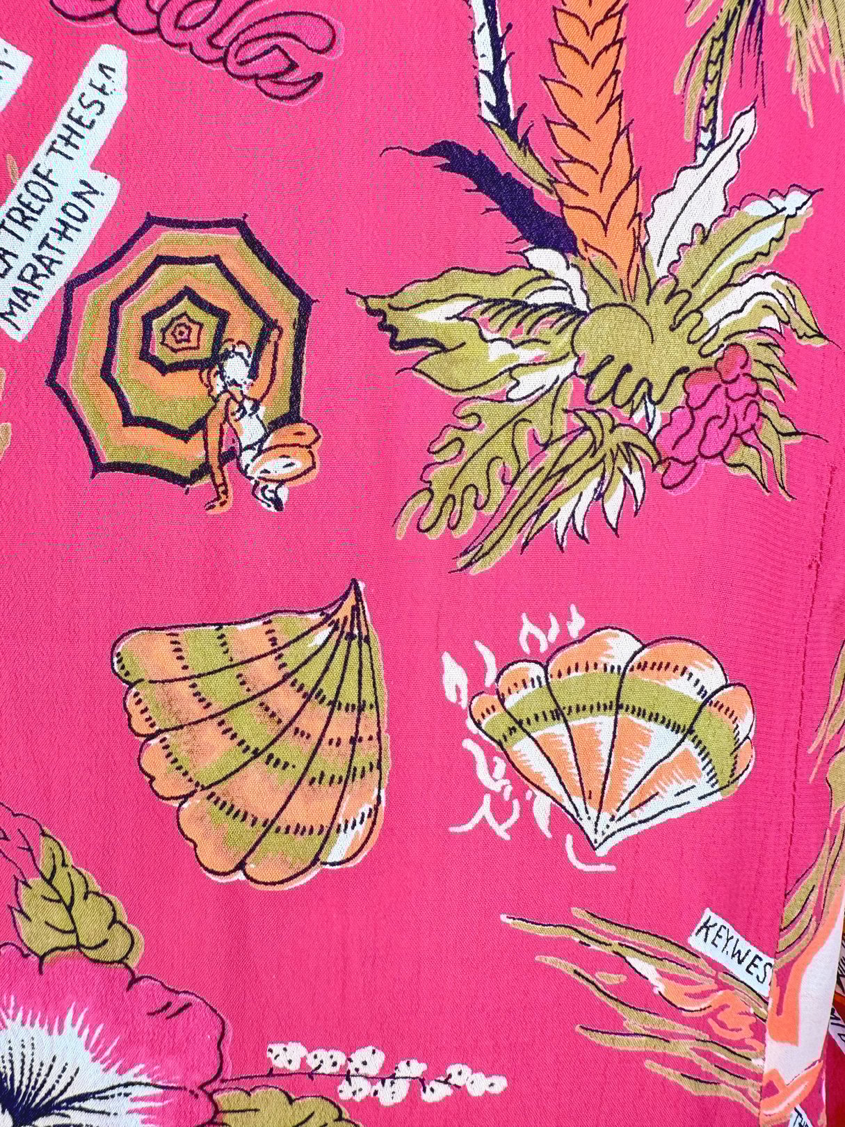 A women's 1970s top in a bright pink fabric featuring tropical motifs such as seashells, palm leaves, and umbrellas.