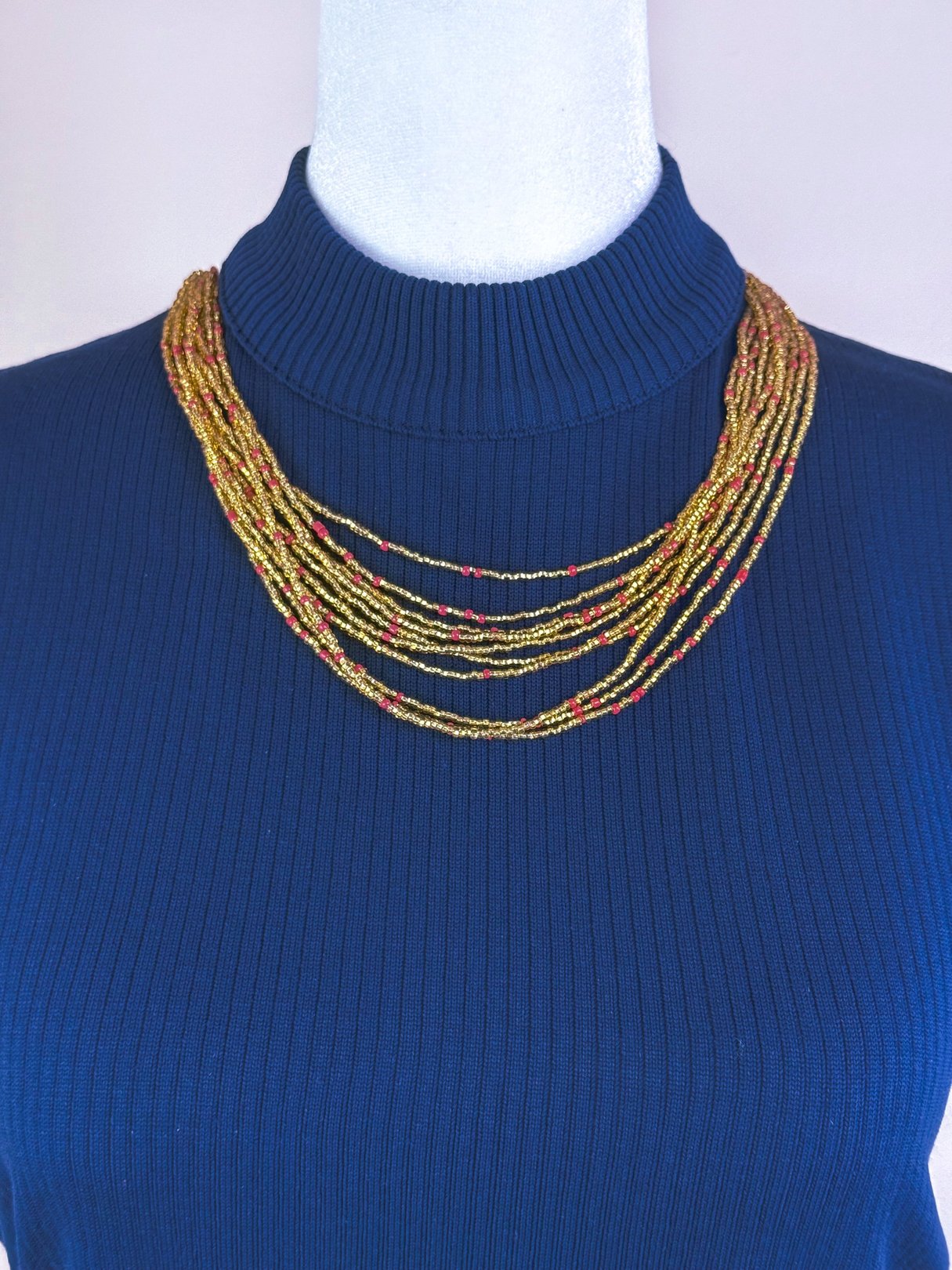 Shimmering gold marigold necklace with layered strands displayed on a mannequin wearing a navy ribbed turtleneck.