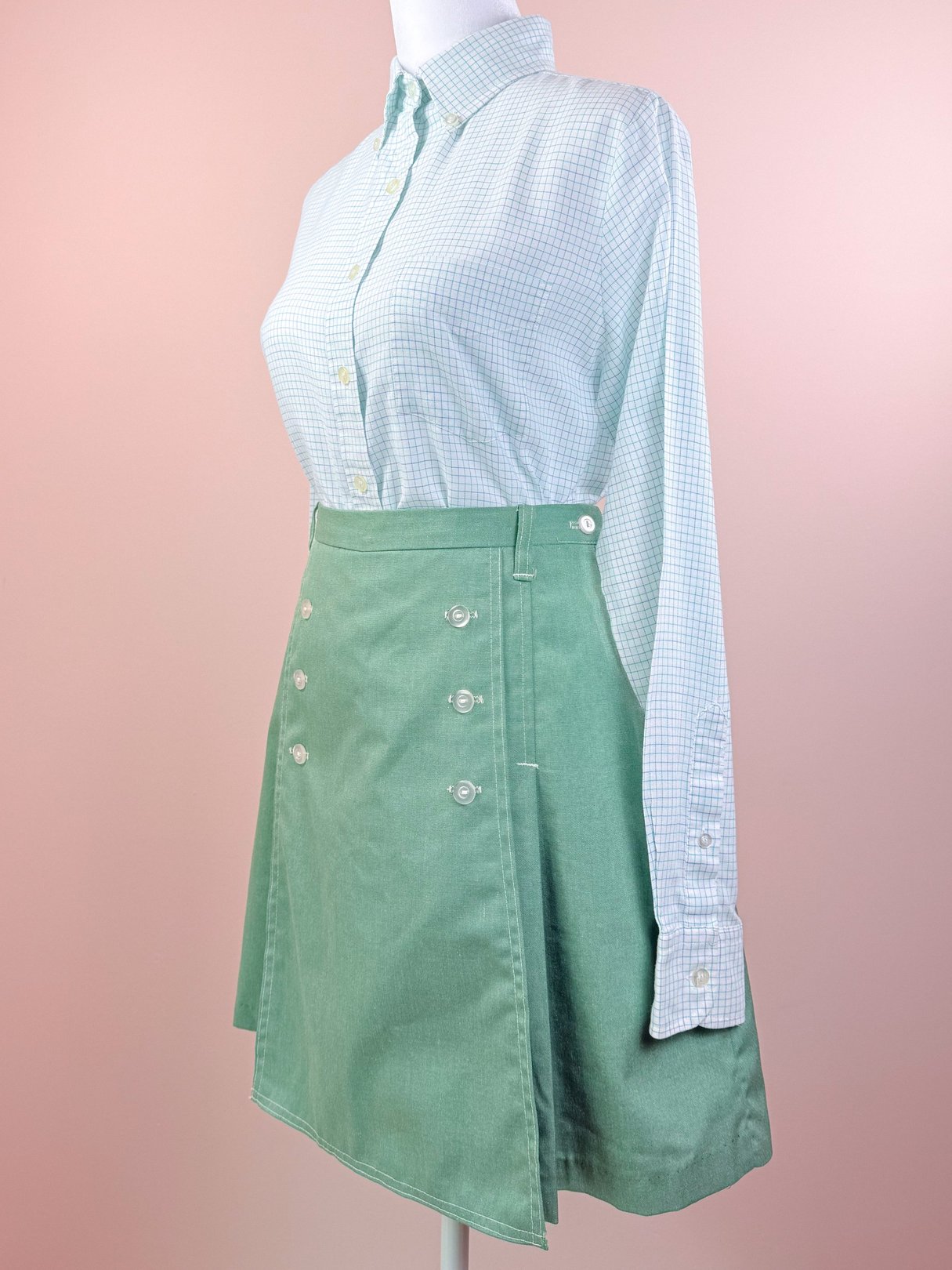 A green 1970s women's skort displayed on a mannequin, paired with a light blue checkered button-up shirt.