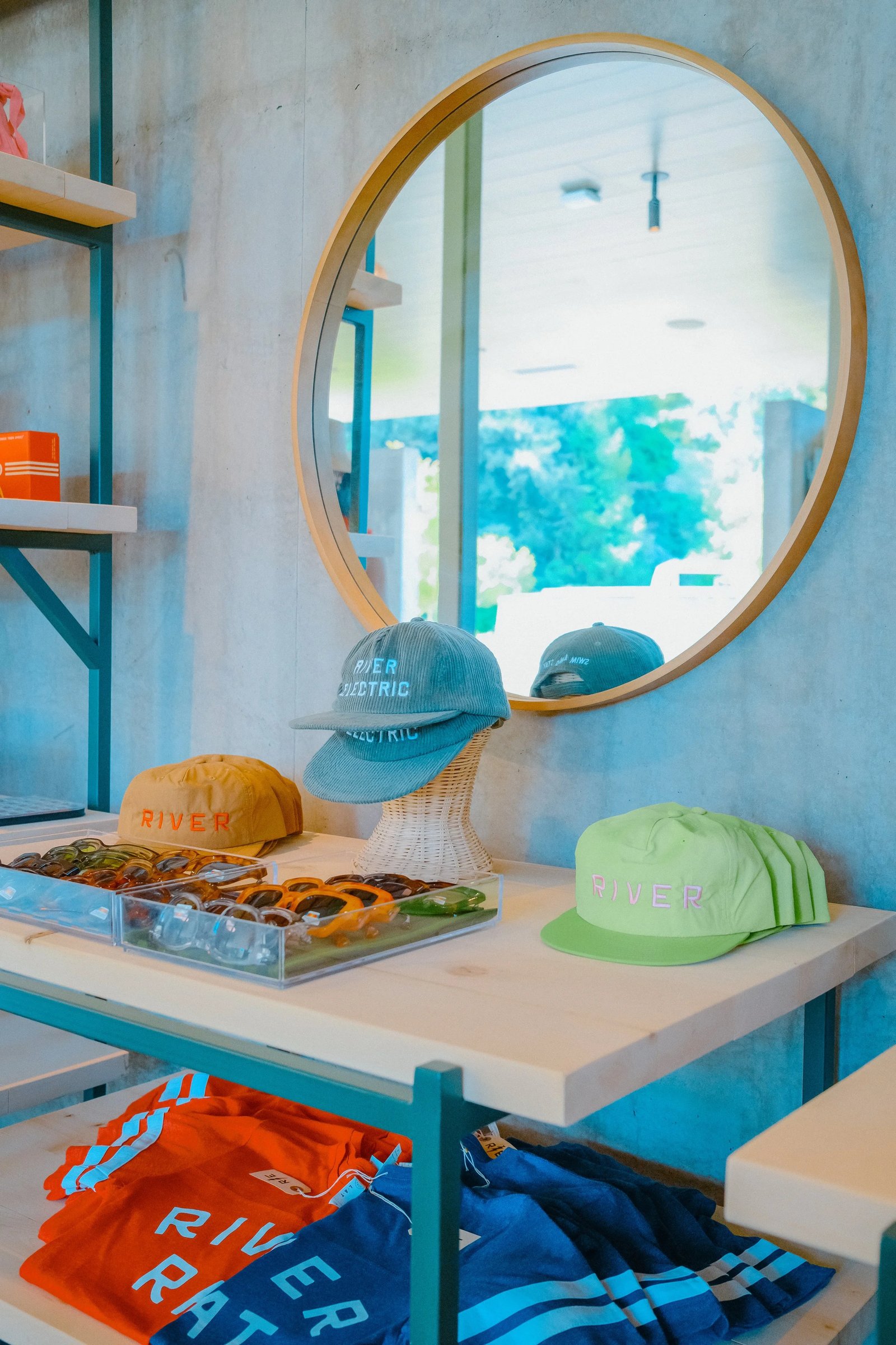 A display of colorful hats and sunglasses on shelves in a boutique with a circular mirror in the background.