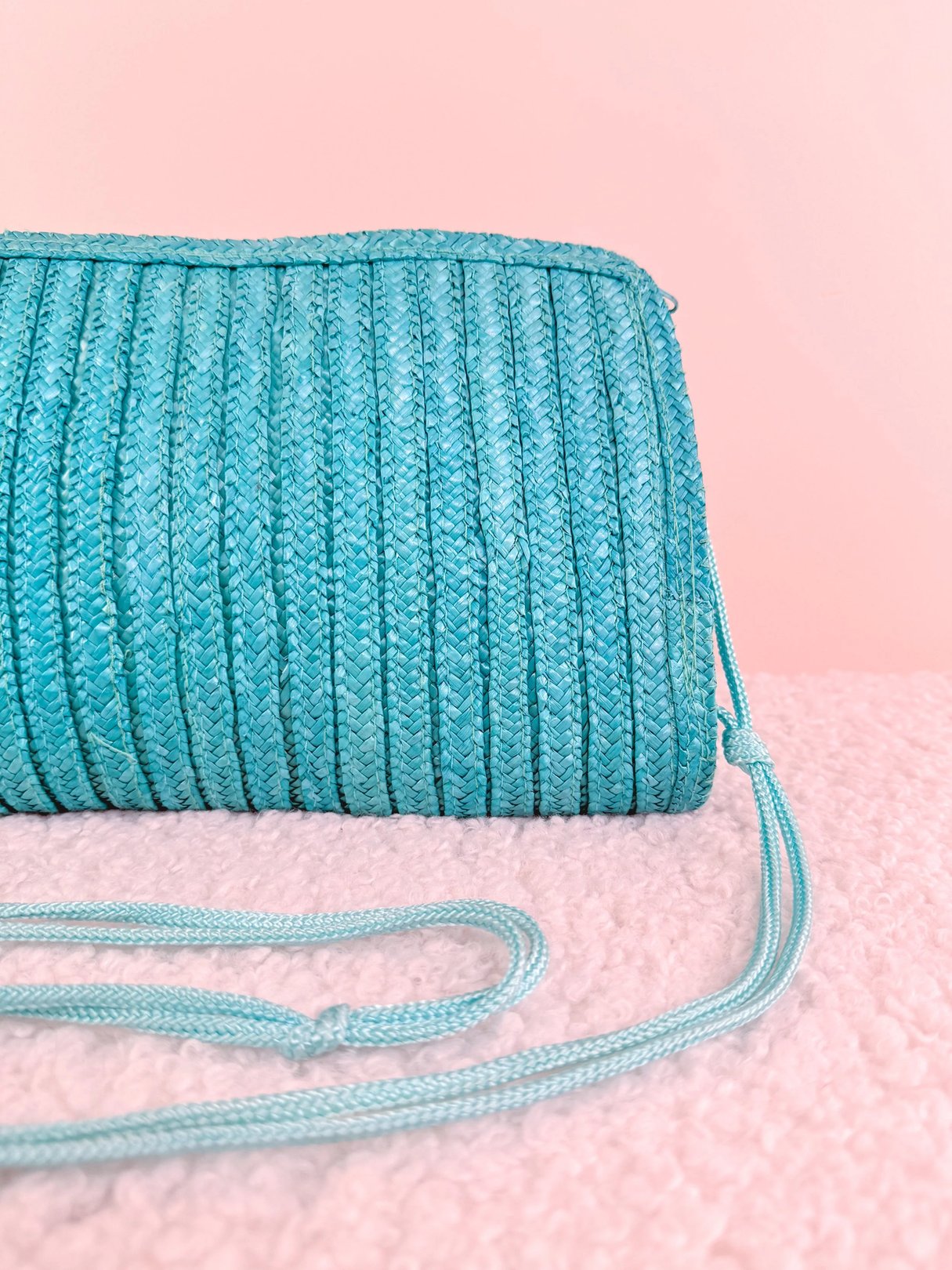 Textured turquoise clutch with a detachable strap against a pink background.