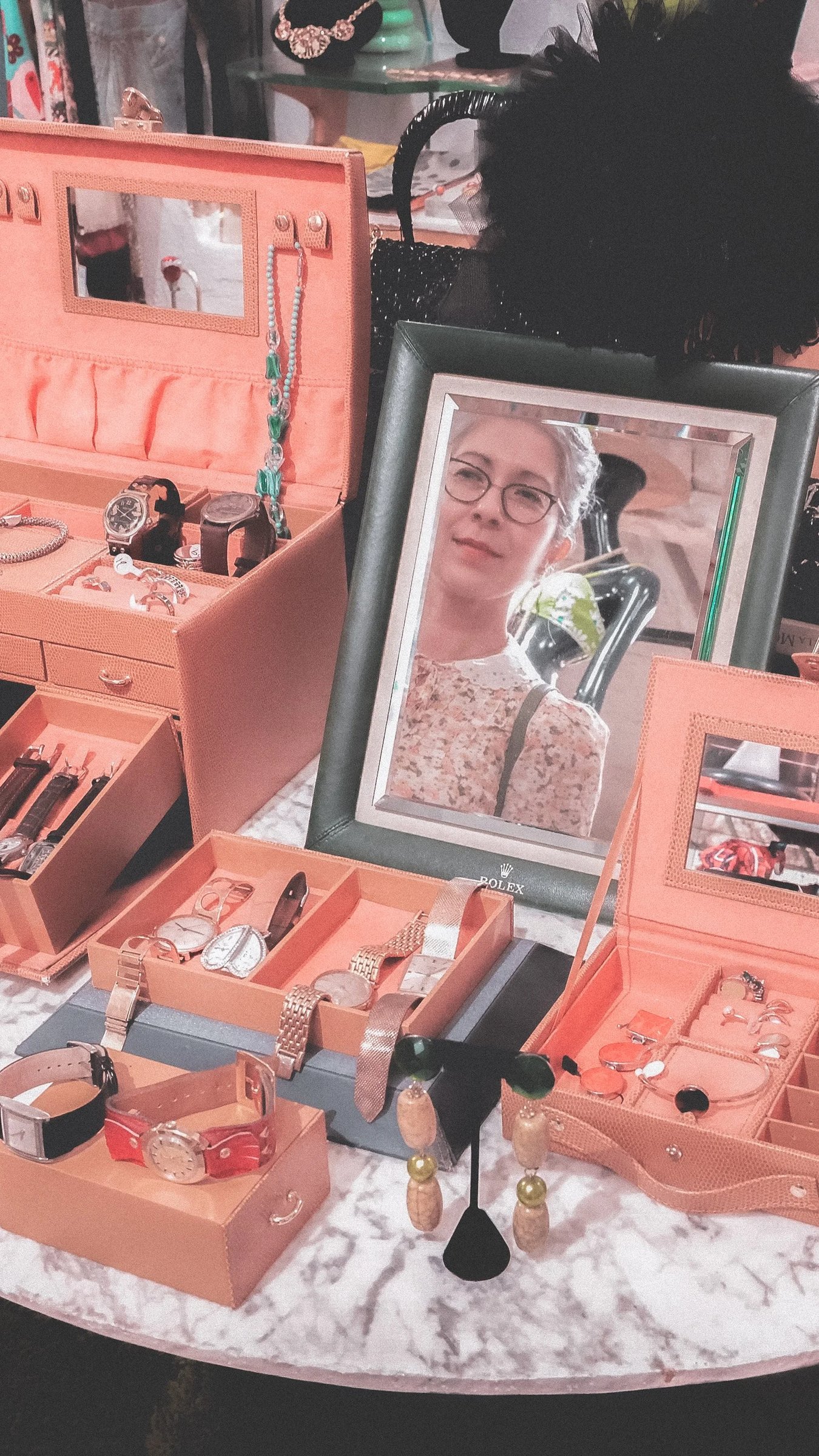 A collection of cosmetics and beauty tools displayed in wooden boxes, with a framed portrait of a woman in the background.