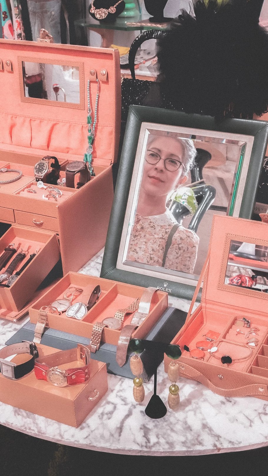 A collection of cosmetics and beauty tools displayed in wooden boxes, with a framed portrait of a woman in the background.