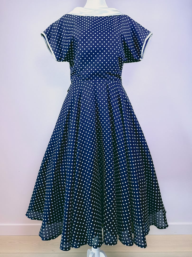 Navy blue, polka dot dress for women from the 1950s featuring a flared skirt and cap sleeves.