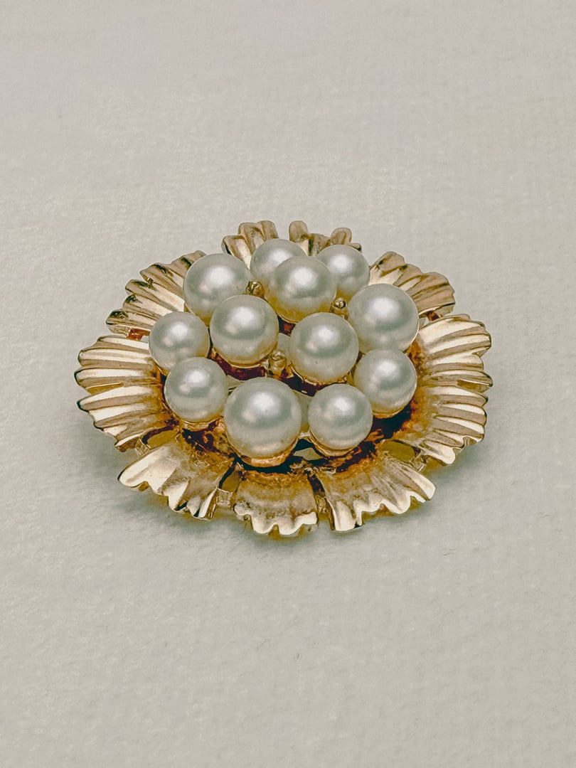 Gold-toned floral brooch featuring multiple pearl embellishments, reflecting 1970s costume jewelry style for women.