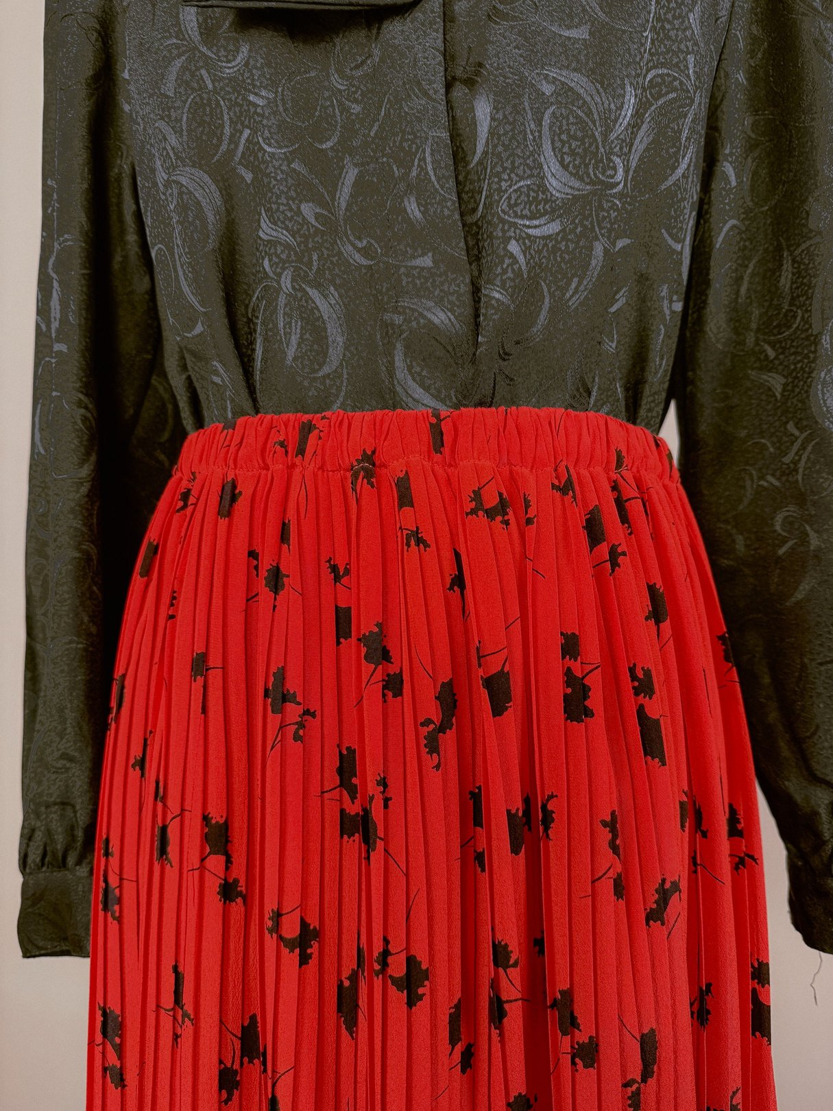 Red pleated skirt with a floral pattern, featuring an elastic waistband, styled with a dark patterned top.