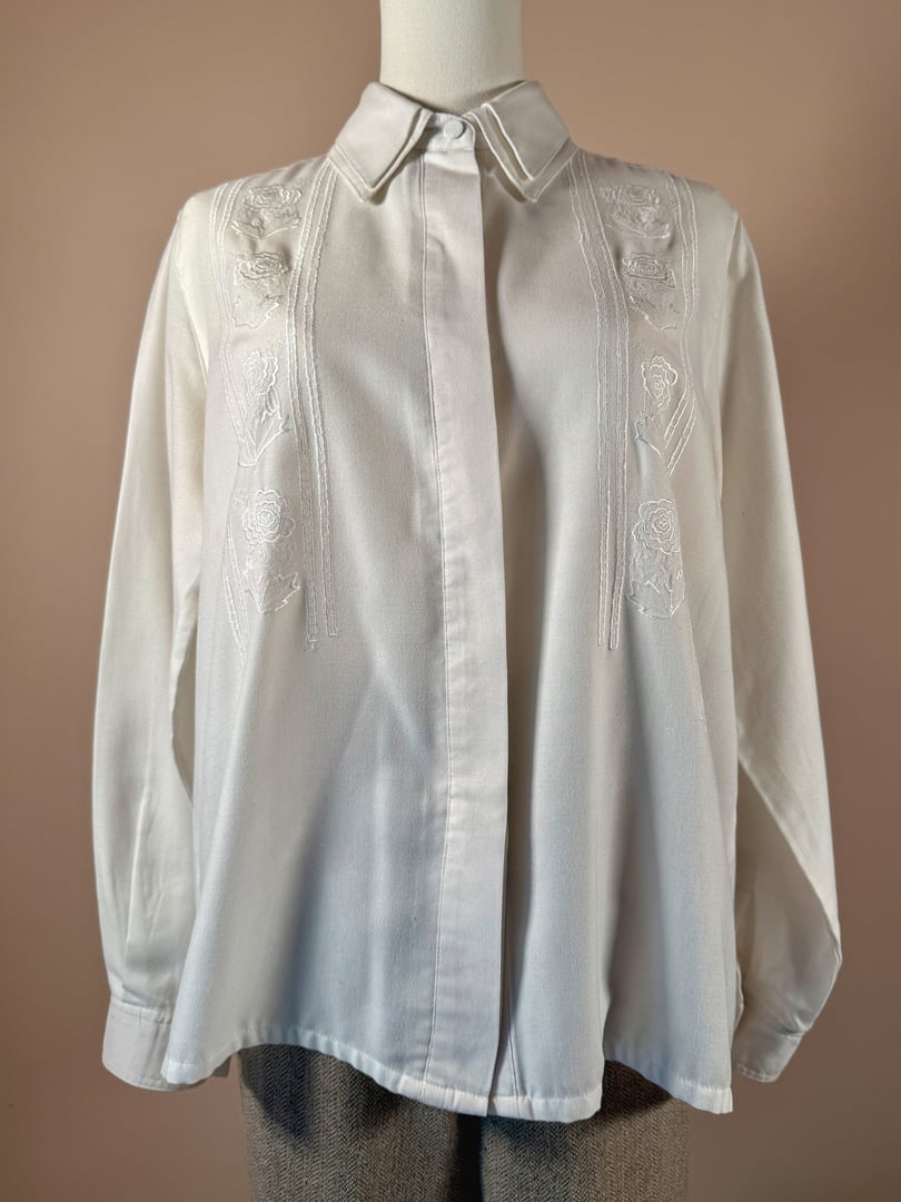 White cotton shirt featuring embroidered floral designs, designed for women, reflecting a 1970s style.
