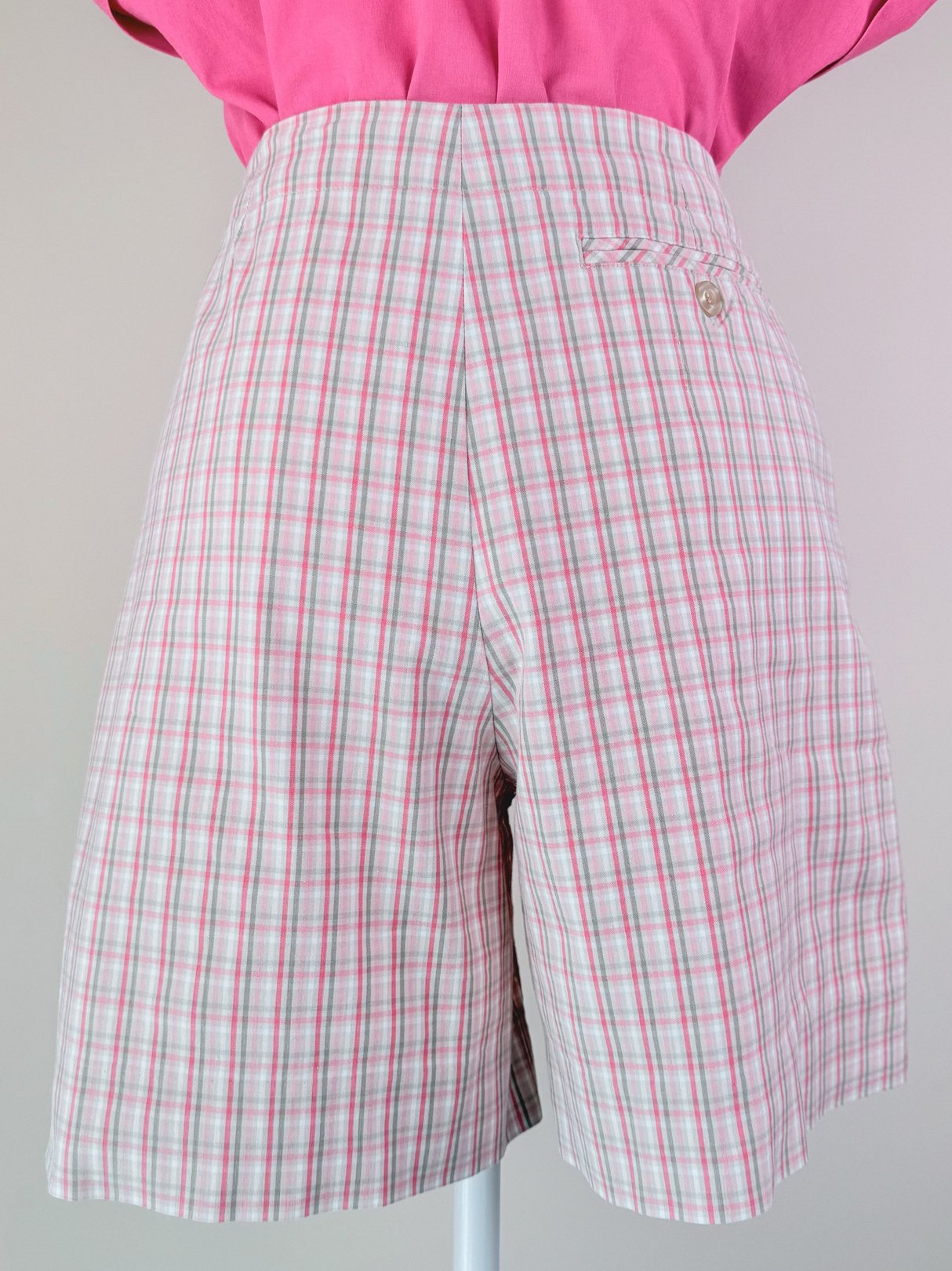 Pink plaid shorts for women, featuring a high waist and a decorative pin, in a 1980s style.