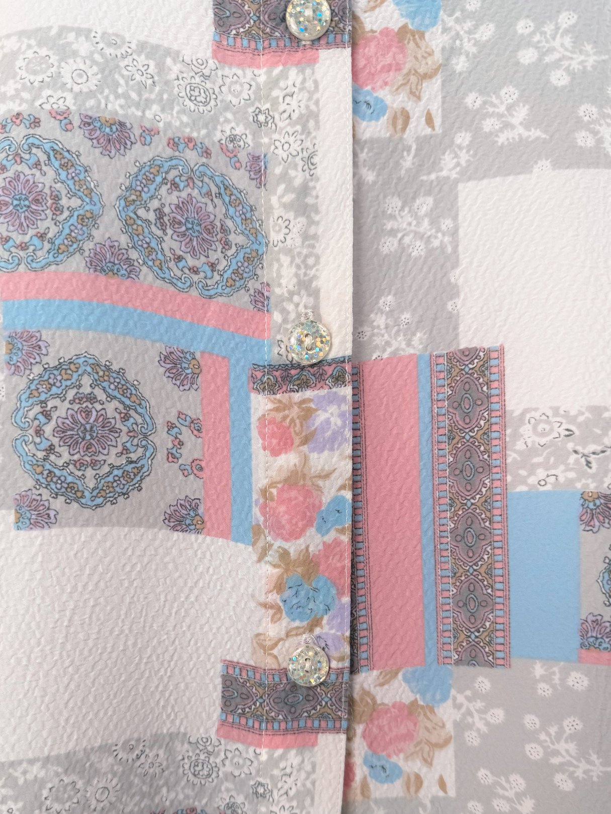 Patchwork Medley Blouse featuring a multicolored patchwork design with floral and geometric patterns, button closure, and a white base.
