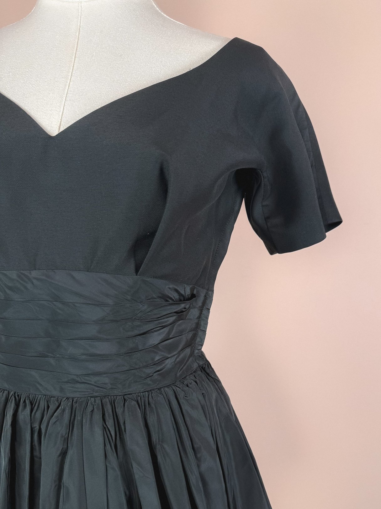 1950s women's black dress featuring a fitted bodice and a full, gathered skirt.