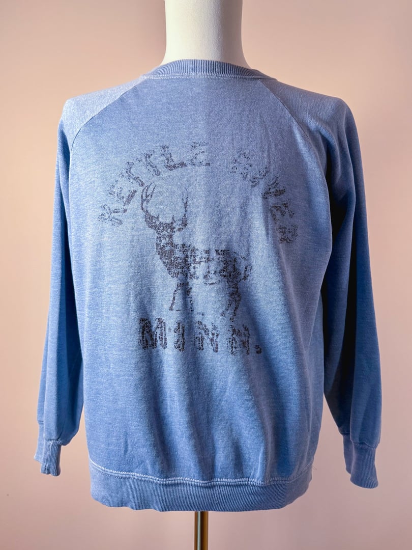 Vintage 1970s blue sweatshirt for men featuring a graphic of a deer and the text "Kettle River Minn." on the back.