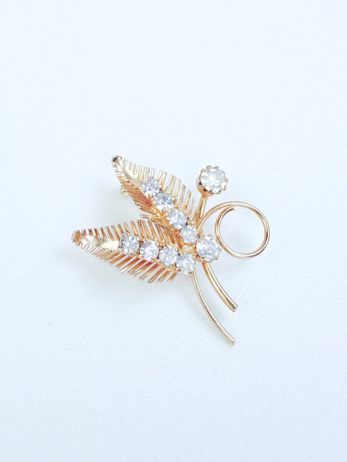 A gold-toned brooch featuring two leaf designs adorned with sparkling rhinestones.