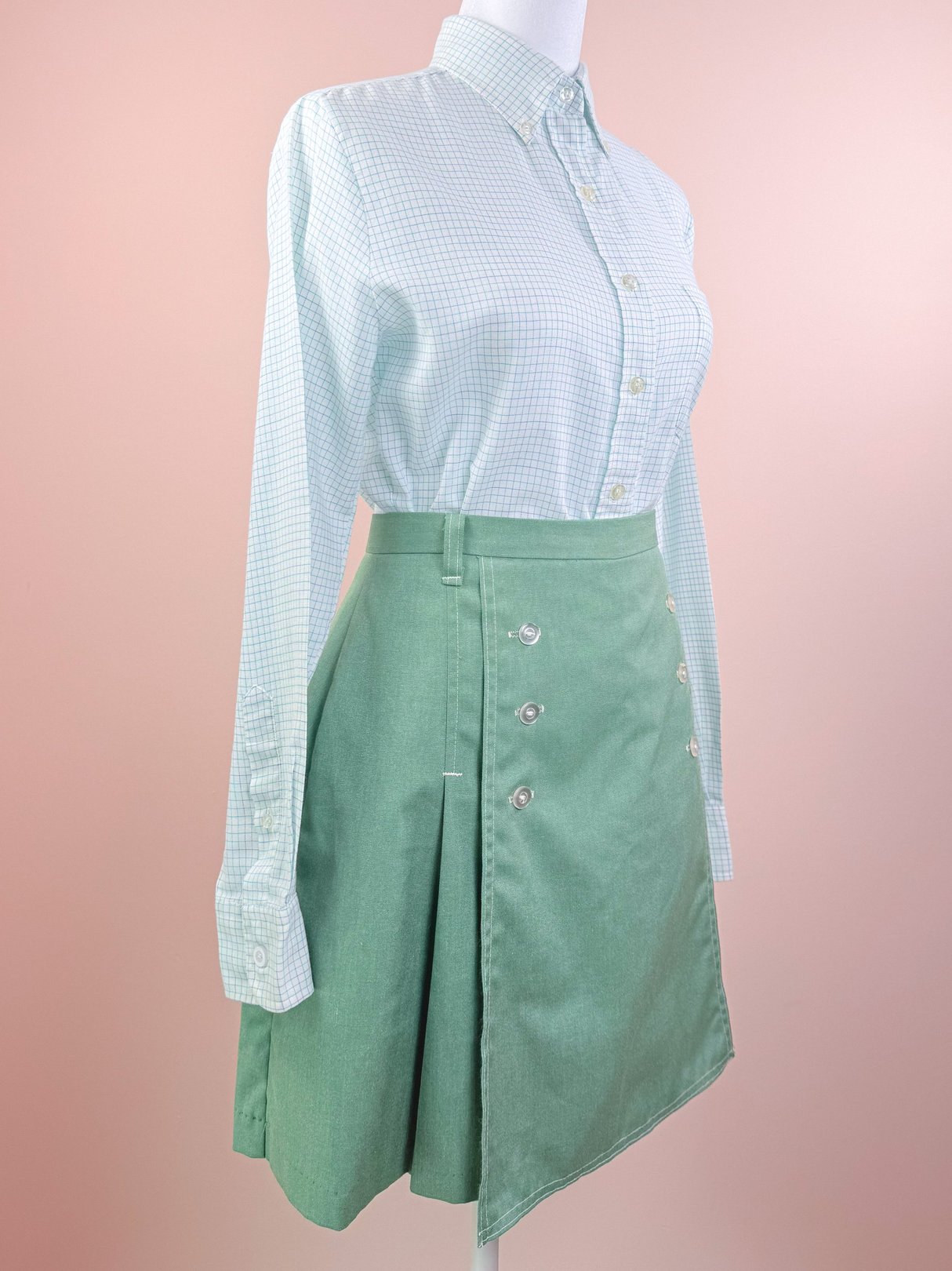 1970s women's skort in green featuring a side button detail, paired with a light blue checkered shirt.