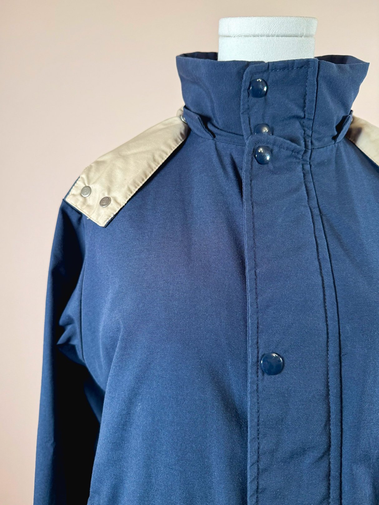 A women's navy blue utility field coat from the 1970s featuring a high collar and contrasting light-colored shoulder details.