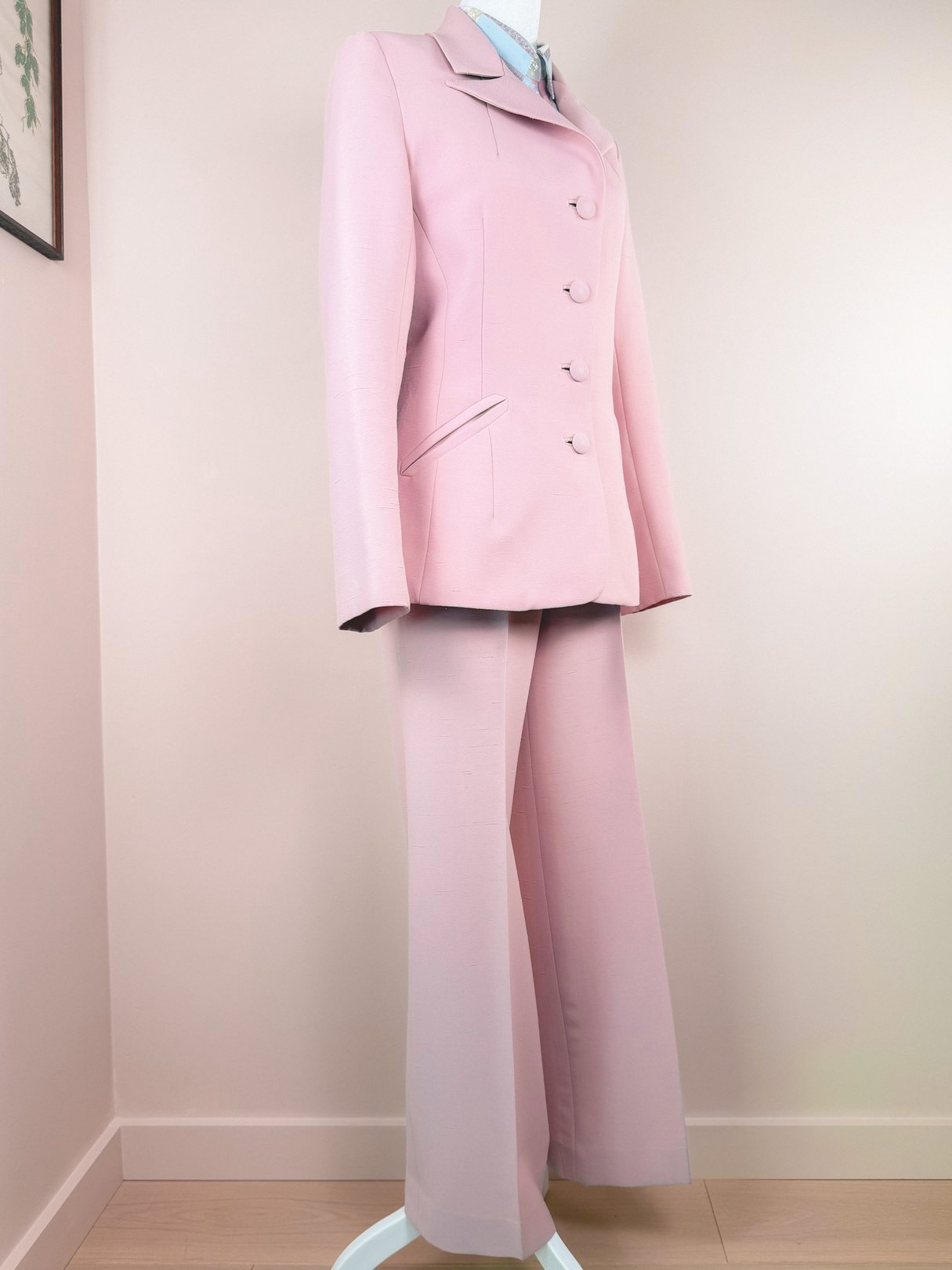 Blush pink 1970s women's three-piece suit featuring a fitted jacket with buttons and wide-leg trousers displayed on a mannequin.
