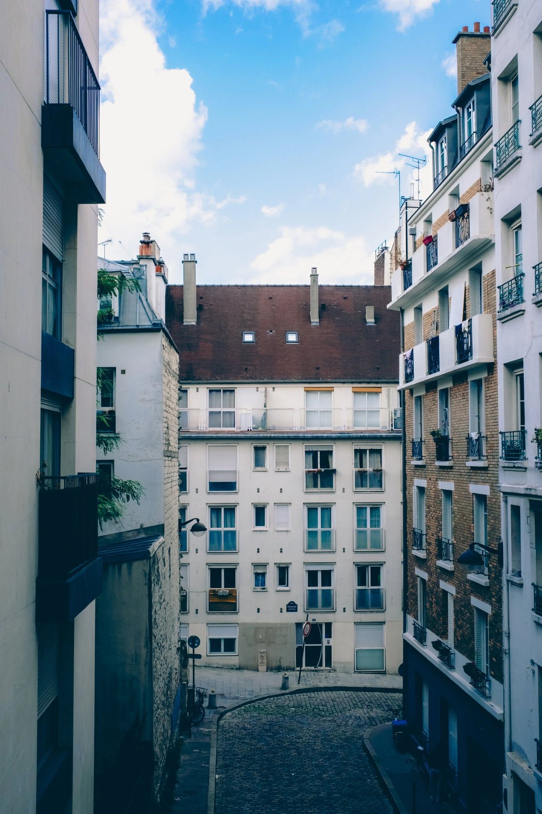 View of a narrow street surrounded by residential buildings with varied architectural styles and a blue sky overhead.