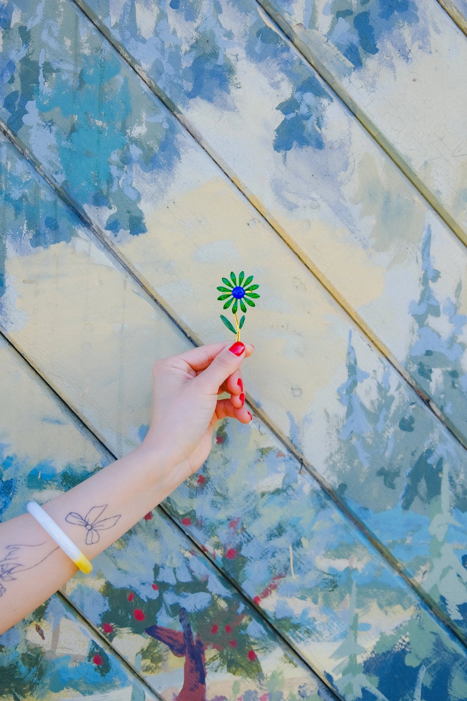 A hand holds a small flower against a colorful, abstract painted background.