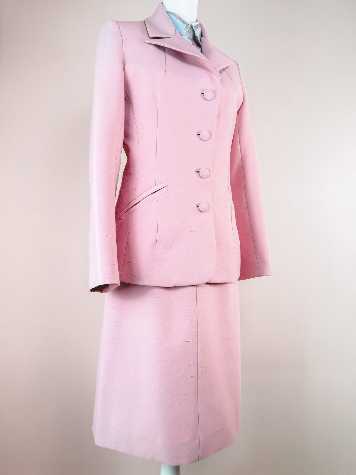 Blush pink three-piece women's skirt suit from the 1970s, featuring a tailored jacket with three buttons and a fitted skirt.