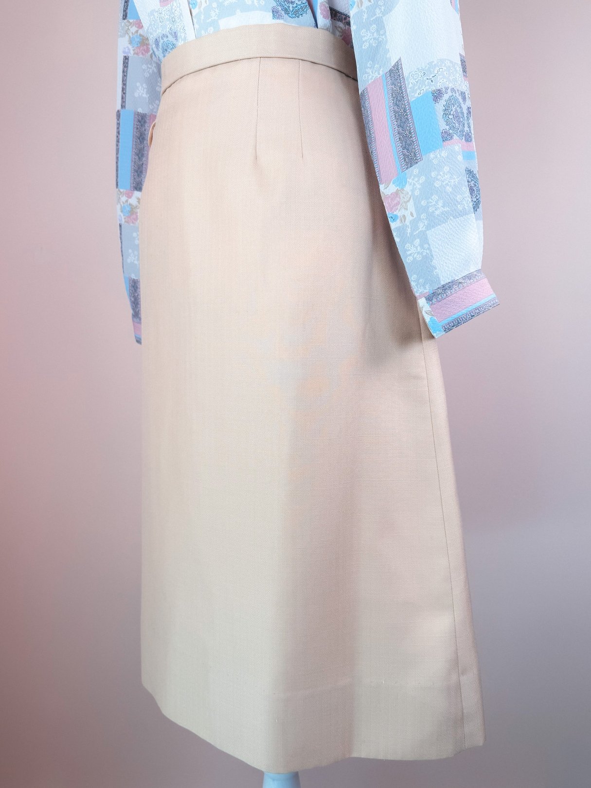 Cream beige women's skirt from the 1960s, featuring a straight silhouette and pleats, displayed on a mannequin against a pastel background.