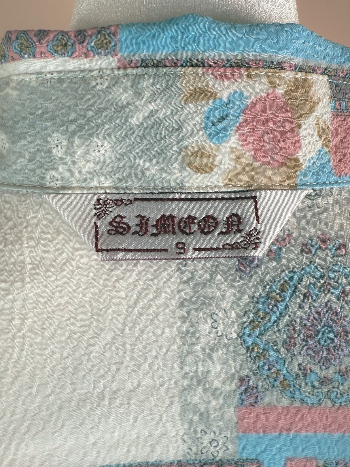White patchwork blouse featuring floral and geometric patterns, with a label showing "SIMEON" and size 9, reflective of 1980s fashion.