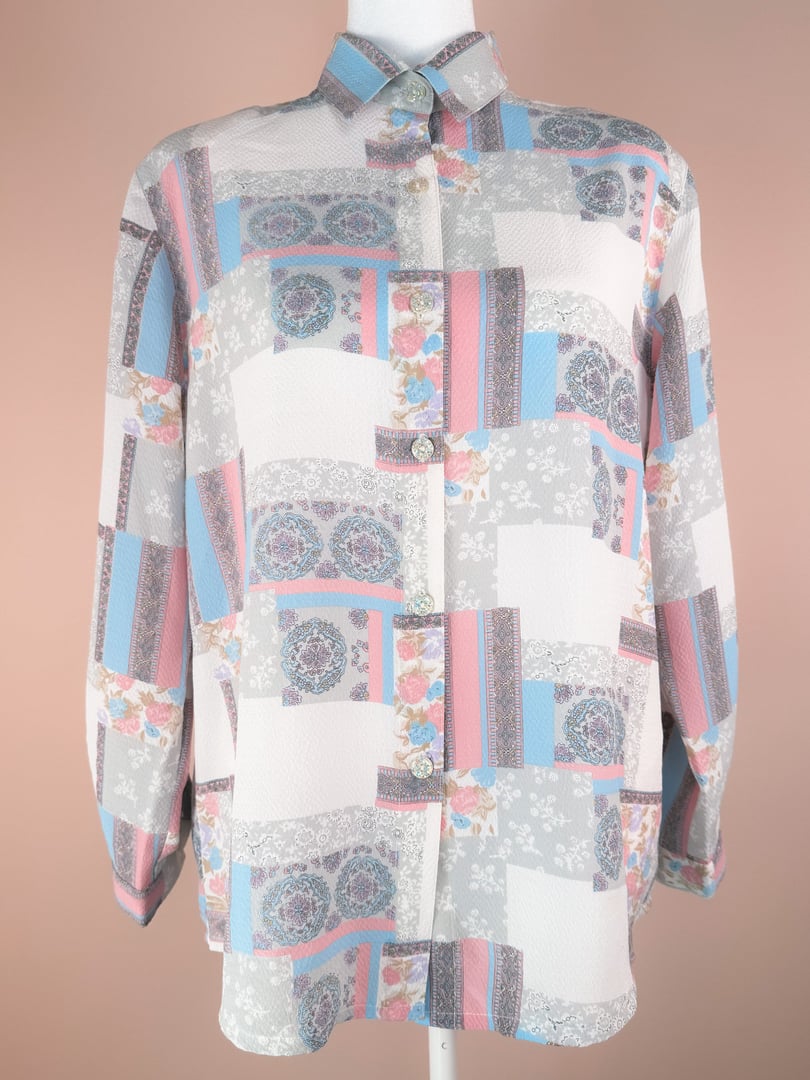 White 1980s-style Patchwork Medley Blouse featuring a multi-pattern design with blue, pink, and gray accents, long sleeves, and a button-down front.