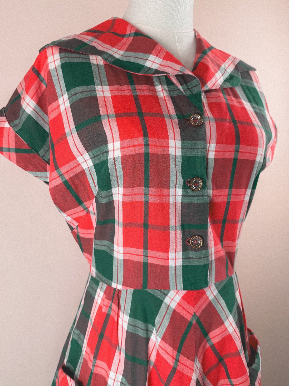 Red plaid dress featuring a wide collar and button closure, reflecting a 1950s style for women.