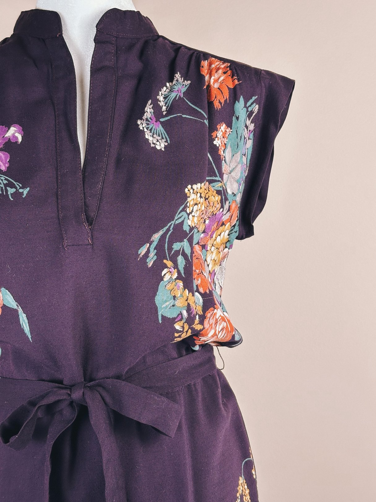 1970s women's purple dress featuring floral patterns and a tie waist.