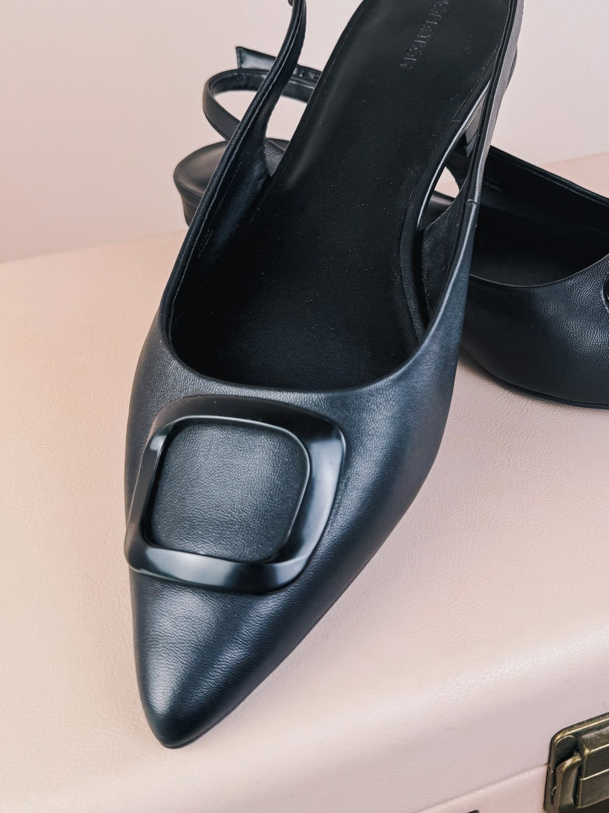 Black 1960s-style women’s slingback flats featuring a pointed toe and a square buckle detail.