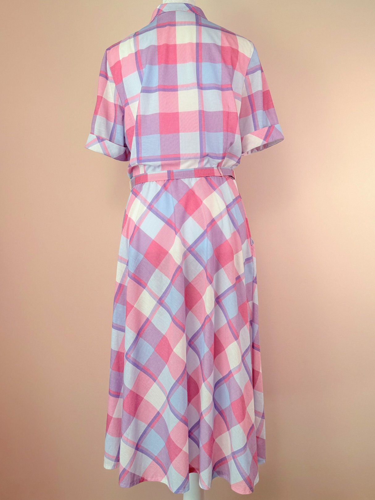 Back view of a 1950s style purple picnic plaid dress featuring short sleeves and a cinched waist, displaying a pattern of pink and purple checkered squares.