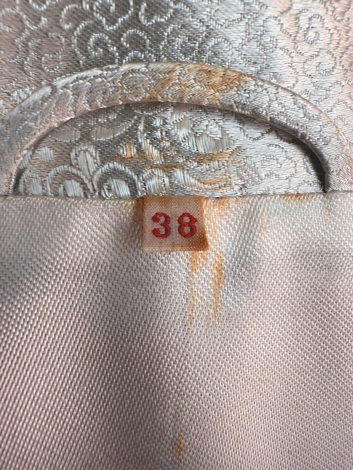 Silver 1970s silk cheongsam coat for women with a tag displaying the size 38.