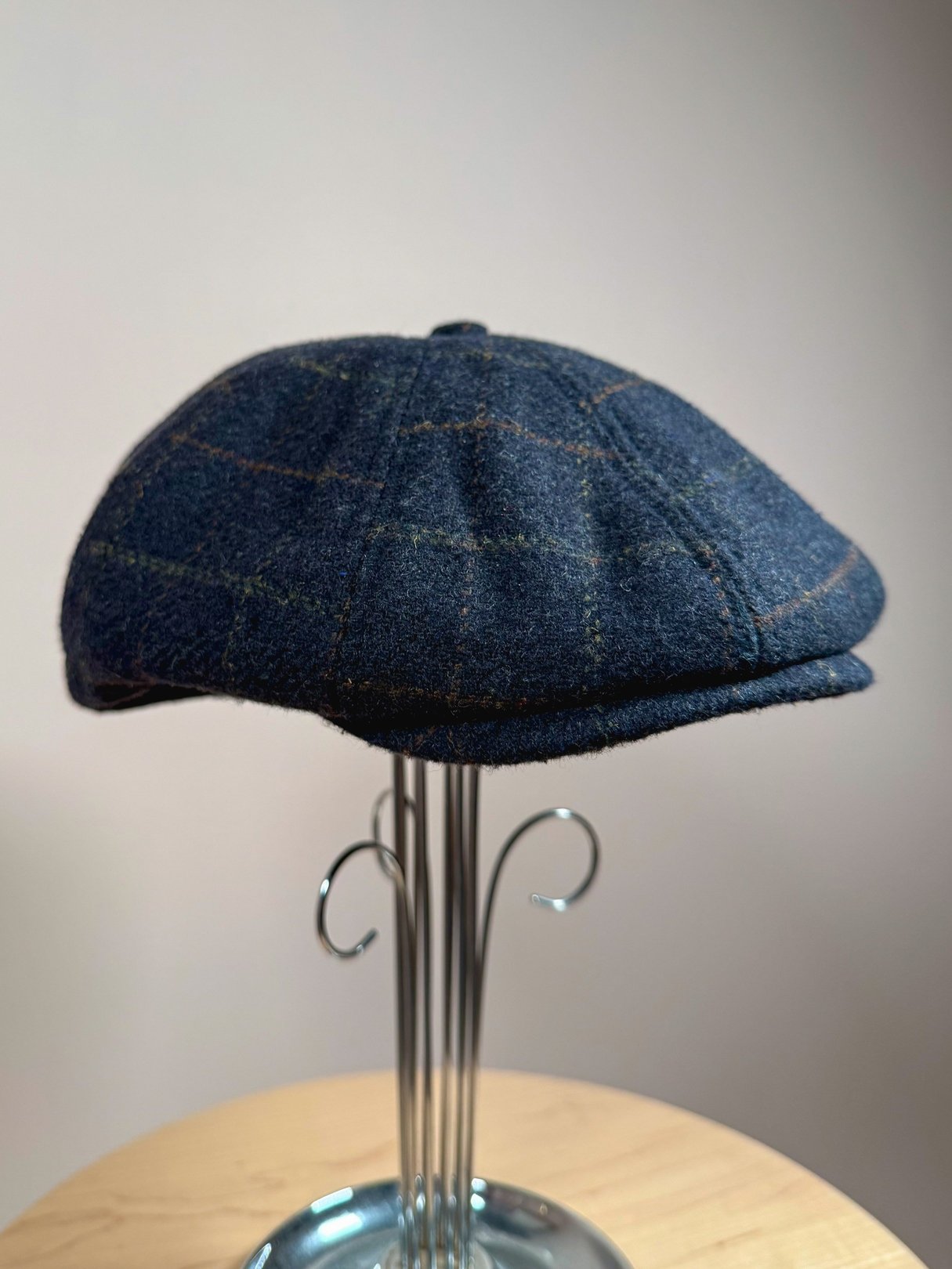 Navy blue tweed cap with a rounded top and plaid pattern, designed for men, reflecting 1970s fashion.