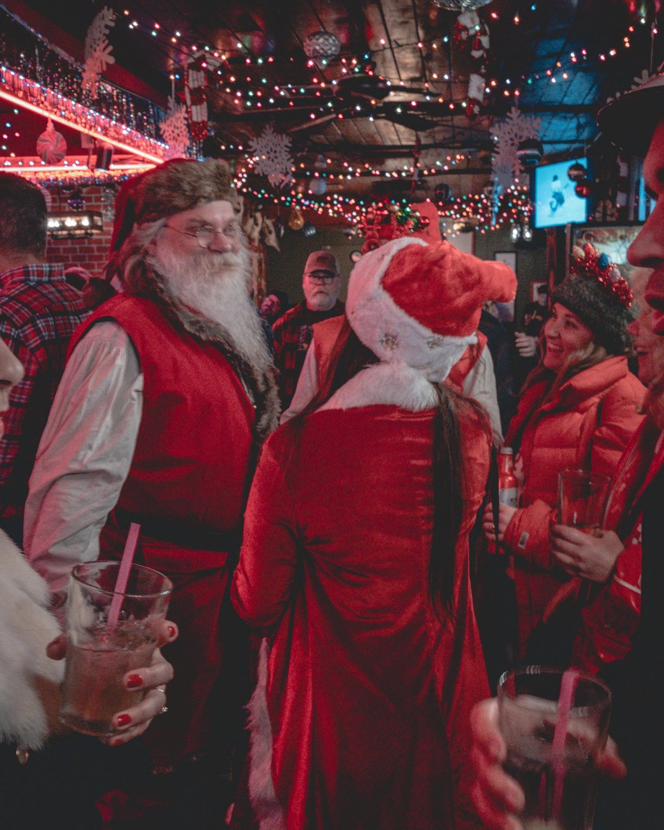 A festive gathering with people wearing Santa costumes and holiday attire in a lively bar atmosphere.
