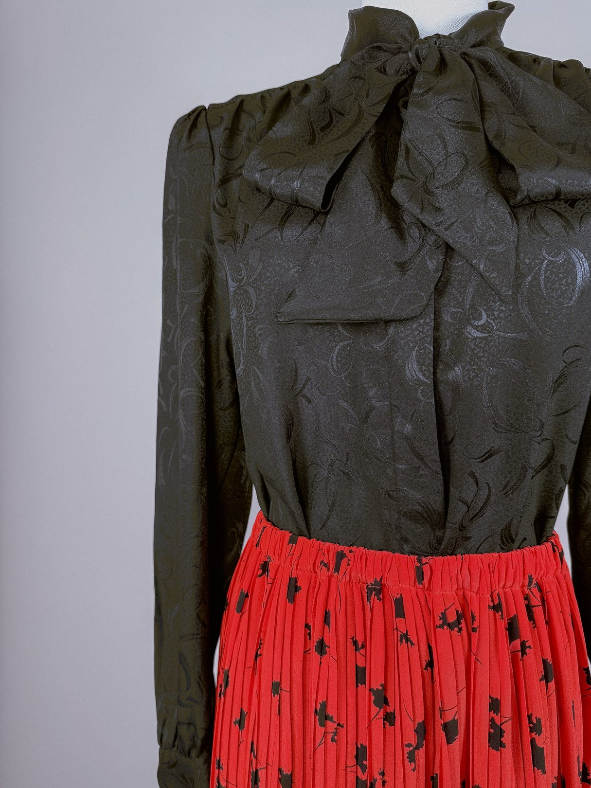 A 1970s women's pleated skirt in red with a floral pattern, paired with a black blouse featuring a bow tie collar.