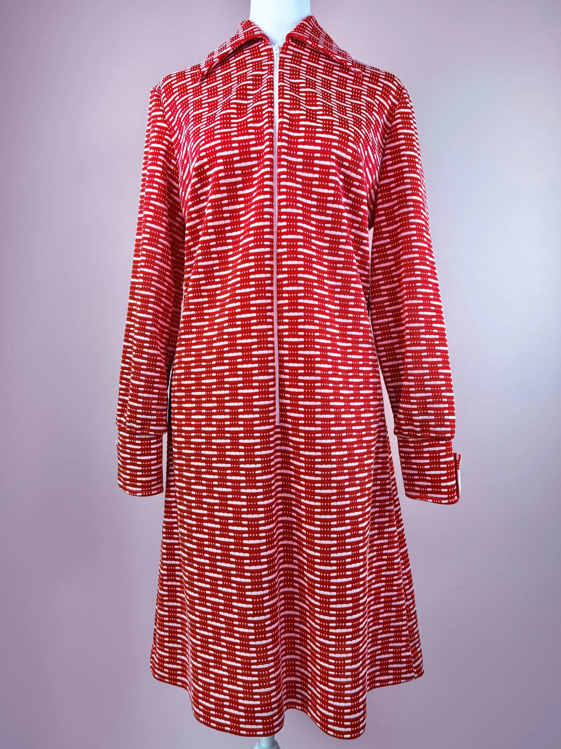 Red patterned dress featuring a zip front and long sleeves on a mannequin against a pastel background.