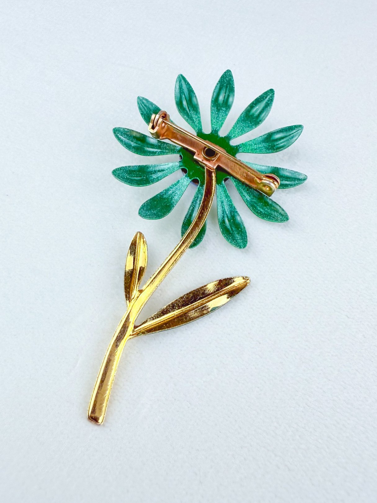 A 1960s blue and green floral brooch featuring a gold-tone stem and leaves.