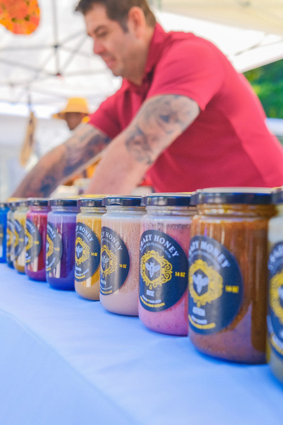 A vendor showcases a variety of colorful honey jars on a table at a market.